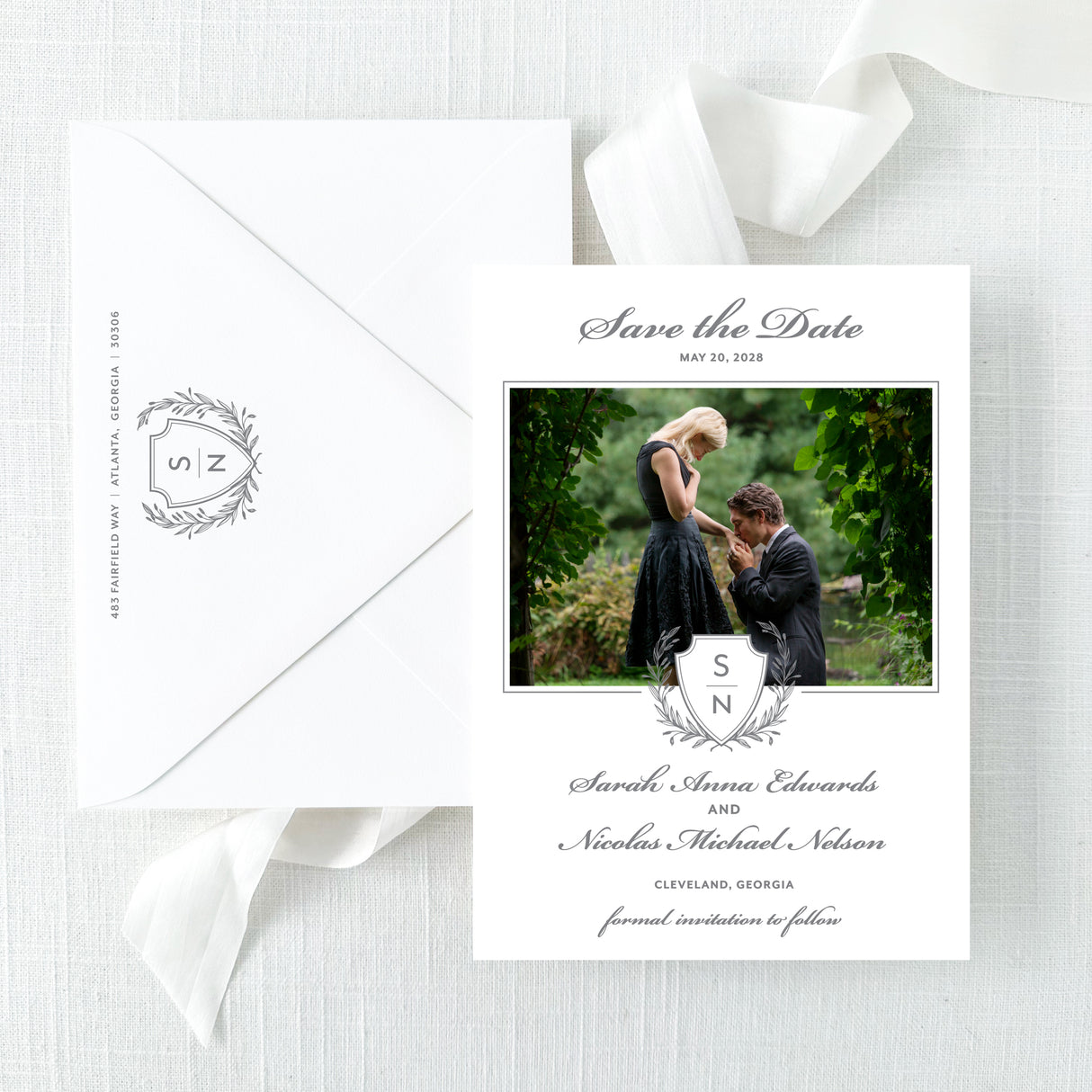 classic wedding save the date card with grey monogram crest and photo of couple with white envelope printed with return address