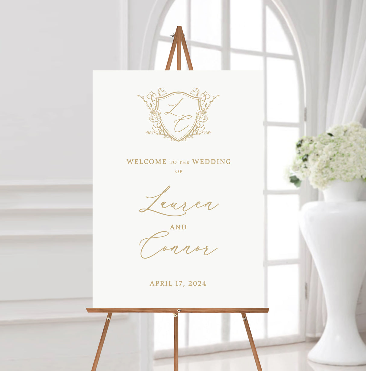 white and gold wedding welcome sign featuring a monogrammed crest at the top and the names of the couple in flowing calligraphy script fonts