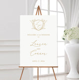 white and gold wedding welcome sign featuring a monogrammed crest at the top and the names of the couple in flowing calligraphy script fonts