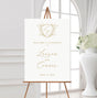white and gold wedding welcome sign featuring a monogrammed crest at the top and the names of the couple in flowing calligraphy script fonts