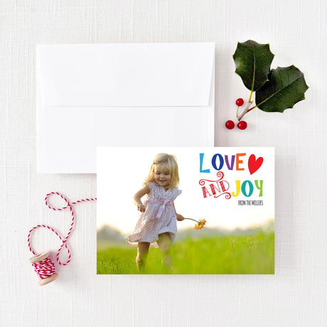Christmas holiday card featuring 'love and joy' text in a fun and colorful font with white square flapped envelope