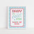 sign with blue, red, and green text 'Baby it's cold outside warm up here' on a light blue background with snowflakes printed on white cardstock
