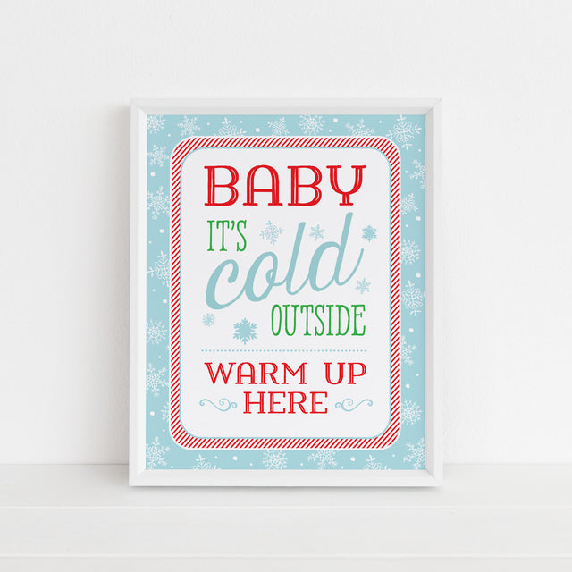 sign with blue, red, and green text 'Baby it's cold outside warm up here' on a light blue background with snowflakes printed on white cardstock