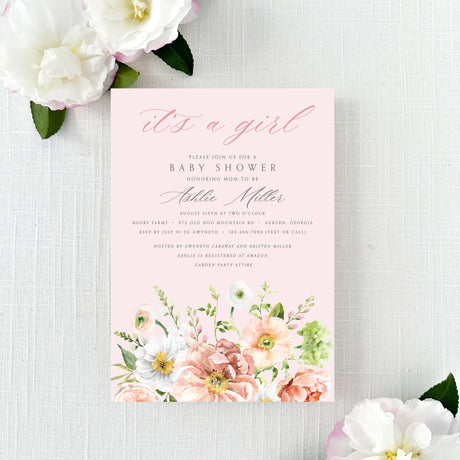 A pink baby shower invitation with floral designs on a pink background