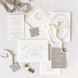 A set of white wedding invitations with hand-torn edges and a minimal wreath design, accompanied by envelopes and RSVP cards, displayed on a linen surface with a grey ribbon.