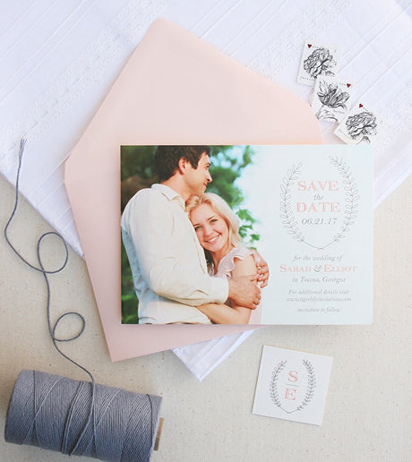 A photo save the date card with a gray and blush laurel wreath design and traditional fonts